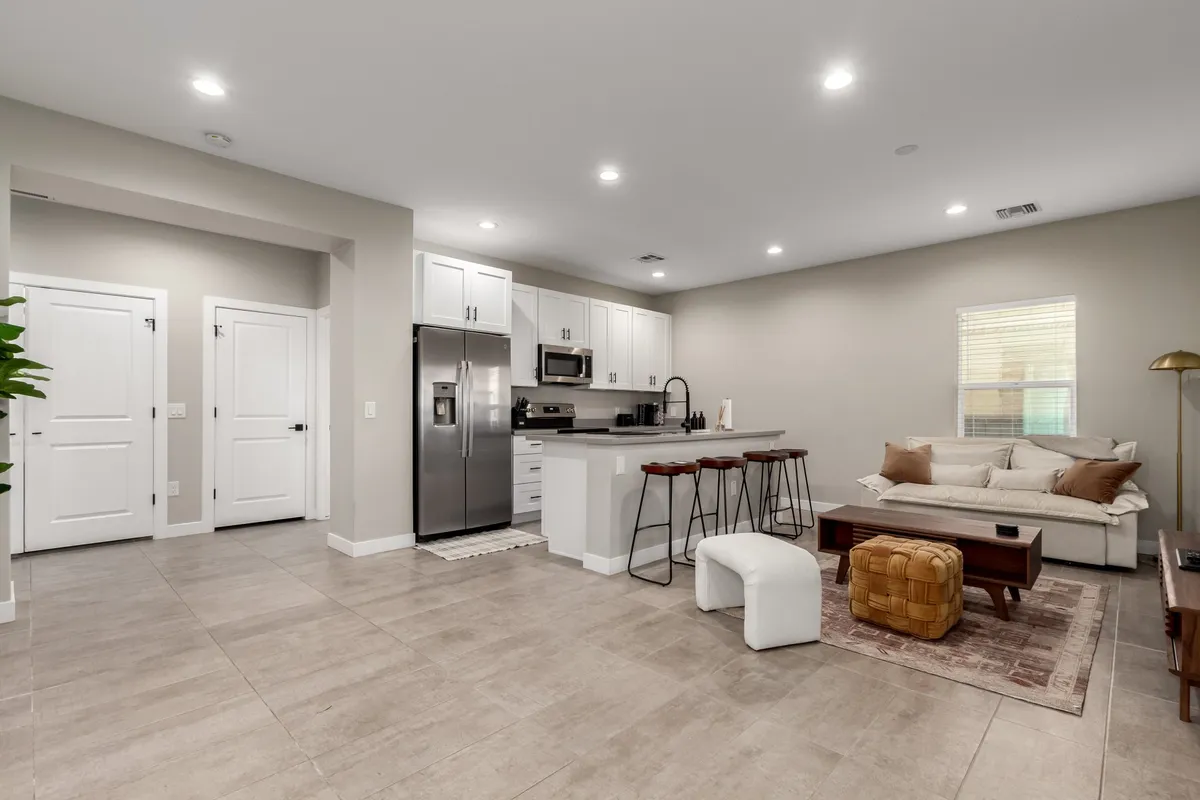This angle reveals the kitchen island adjacent to a sofa and coffee table, capturing the flow between living, dining, and kitchen zones. The scene is lively and inviting, ideal for entertaining, cooking together, and relaxing. Decor choices and abundant light add to the welcoming, family-friendly vibe.