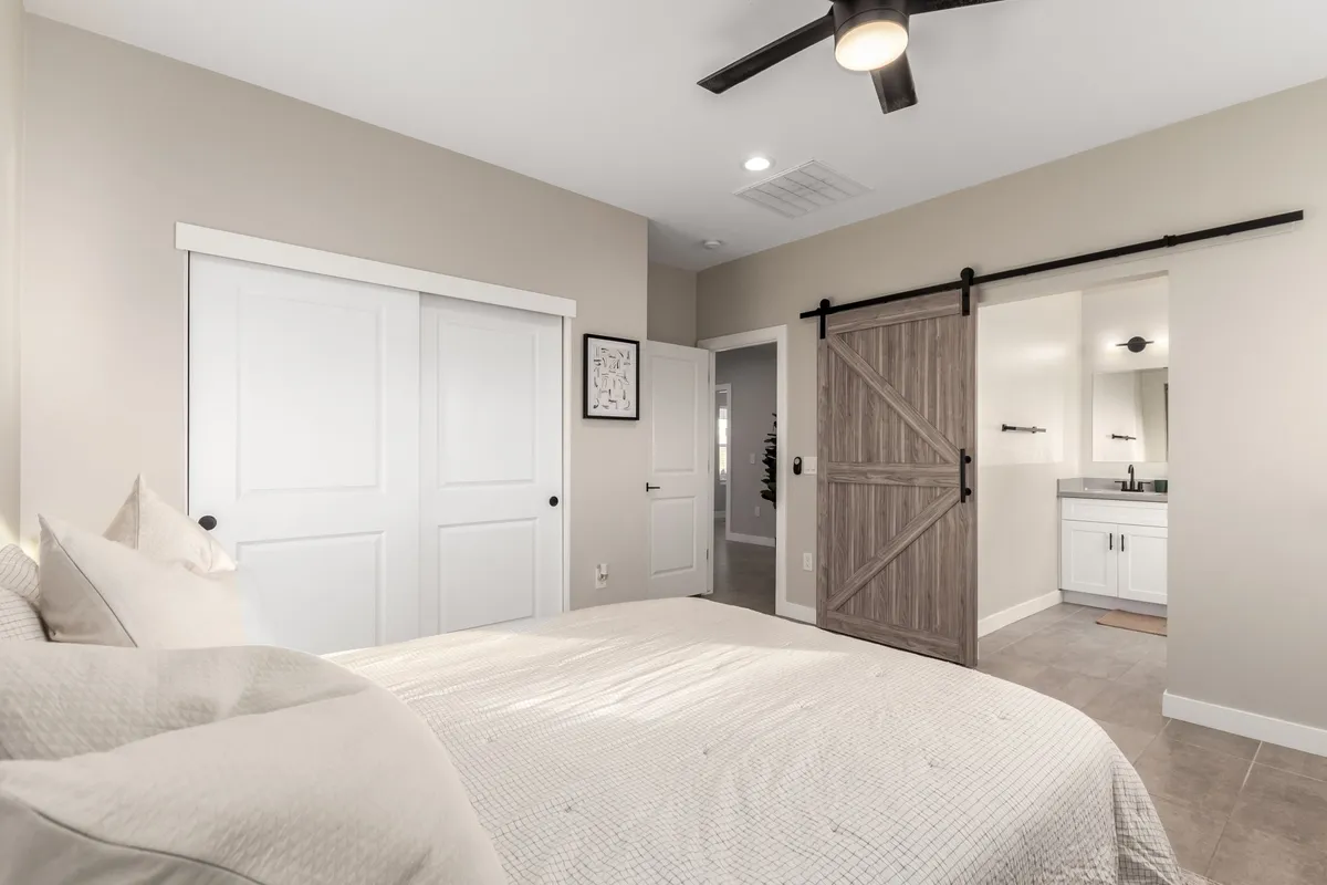This image features a serene bedroom setting with a comfortable bed, a barn door, and a stylish vanity area. The space exudes a calm and inviting atmosphere, ideal for relaxation after a busy day. Natural light filters into the room, enhancing the sense of tranquility and privacy.