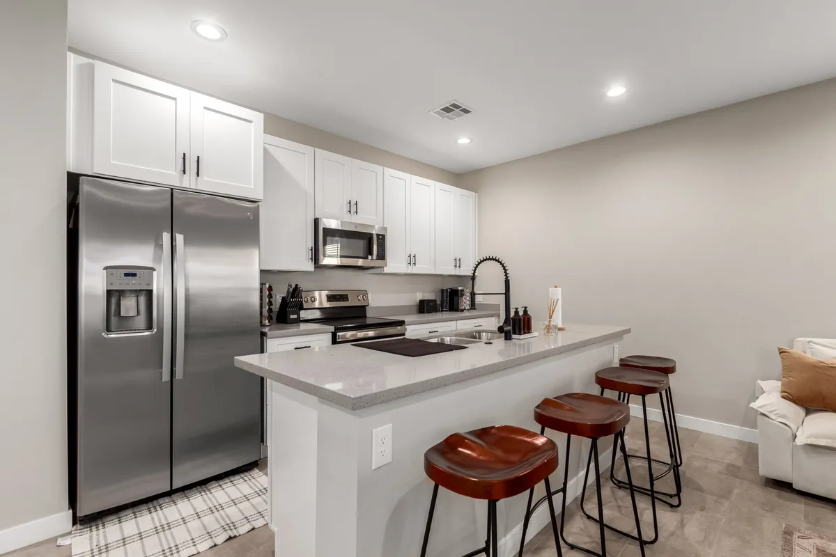 A bright, functional kitchen featuring stainless steel appliances, white cabinetry, a spacious kitchen island with wooden bar stools, and ample counter space. The setting is ideal for cooking, entertaining, or enjoying a casual breakfast, reflecting a clean and modern style.
