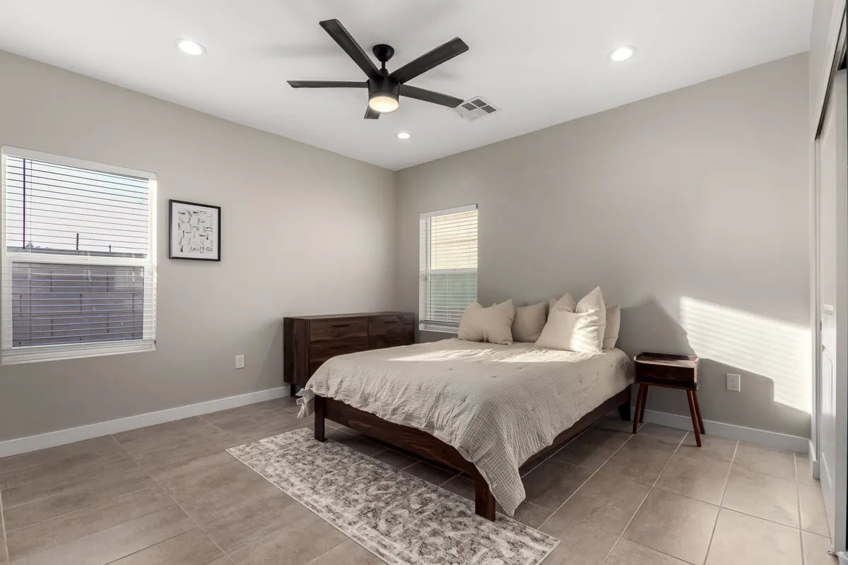 A tranquil bedroom with a comfortable bed adorned with decorative pillows, a cozy nightstand with a lamp, and framed artwork on the wall. The space is softly lit, evoking a restful and inviting atmosphere.