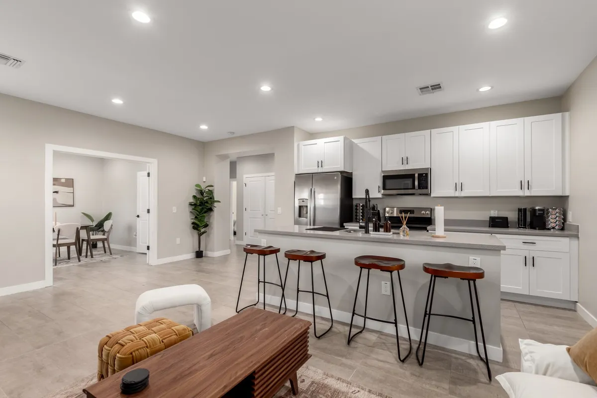 An inviting open-plan space showcasing a modern kitchen island with bar stools, seamlessly flowing into a cozy dining area. The area is accented by an indoor plant and is styled for both cooking and gathering, emphasizing social interaction and comfort.