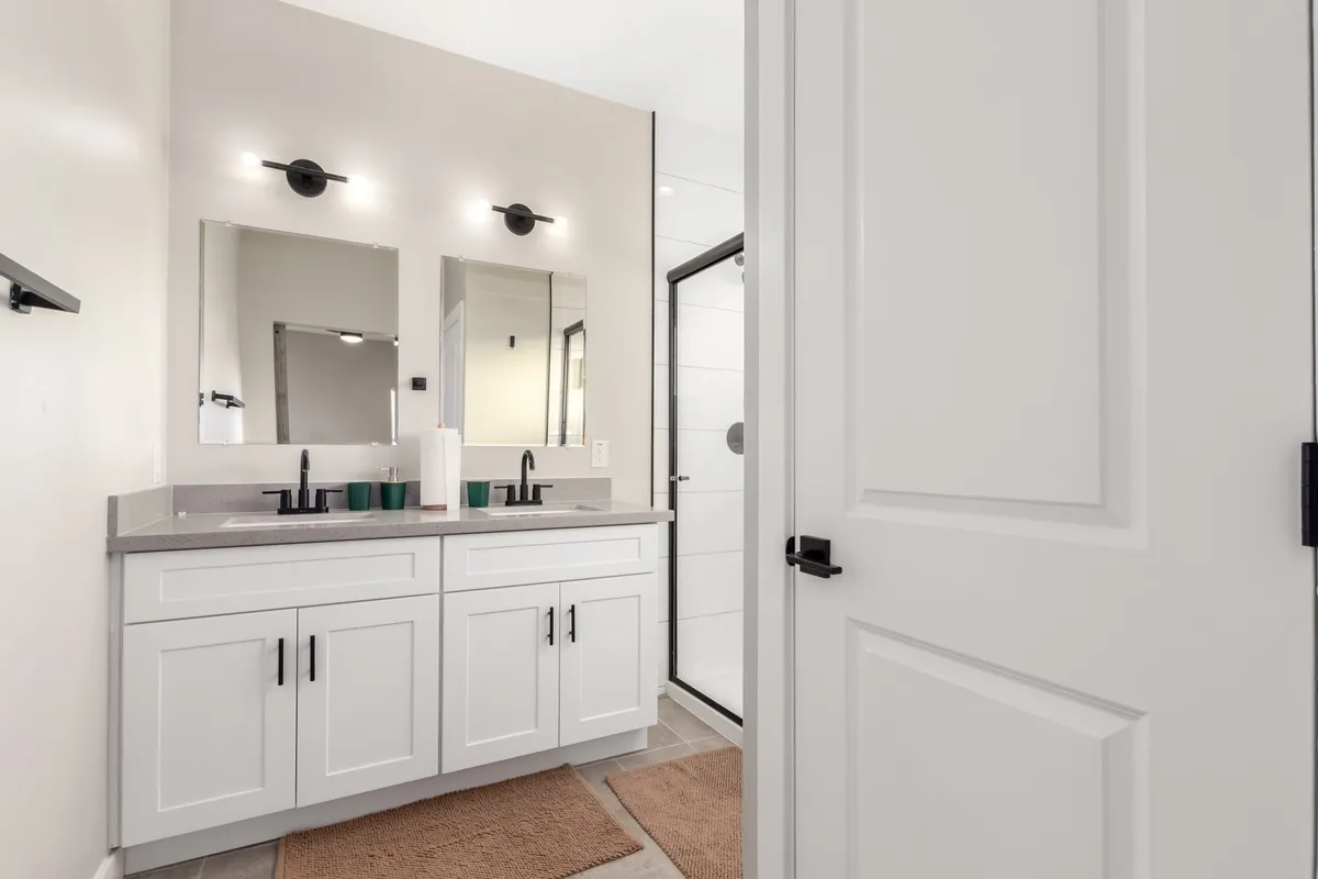 A fresh, modern bathroom featuring a double vanity with two sinks, large mirrors, and a spacious shower area. The room feels bright and inviting, ideal for morning routines or winding down in the evening.