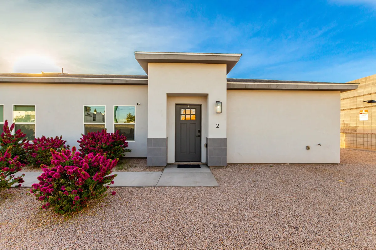 The image features the home's inviting front entryway, framed by flowering shrubs and a welcoming building facade. The front door stands out as the focal point, with well-tended landscaping creating a sense of warmth and comfort. The scene has an inviting mood, suggesting a tranquil spot for enjoying sunsets or greeting guests.